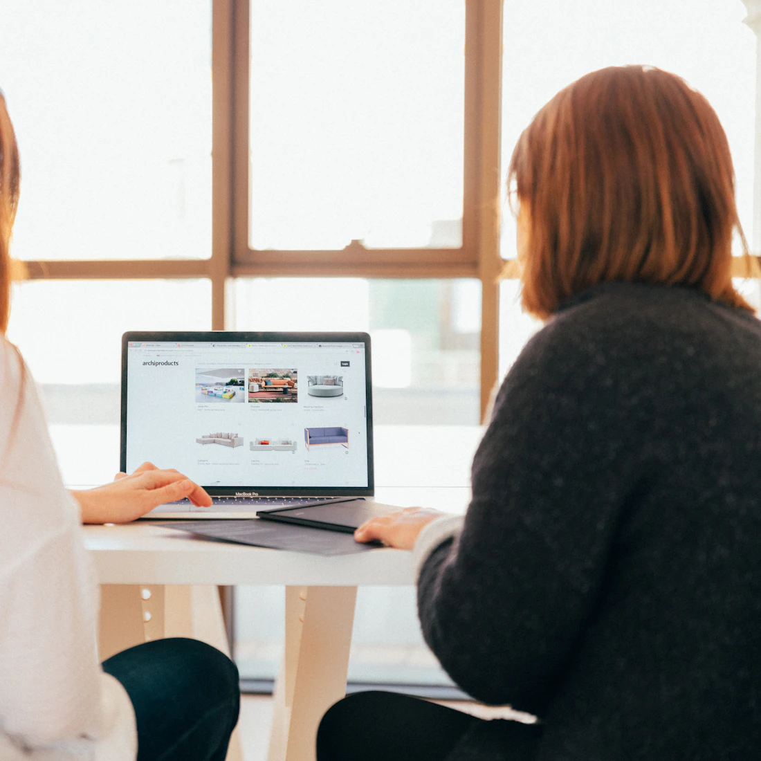 Two colleagues reviewing a website together on a laptop by a bright window